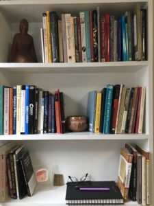 White bookshelves holding books, a journal, glasses, pens, and a ceramic bowl and figure