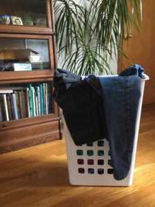 Jeans hanging over full white laundry basket