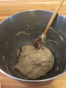 ball of bread dough in bottom of mixing bowl with wooden spoon