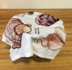 a mixing bowl covered with a damp dishtowel with colorful illustrations of New England Seashells all over it