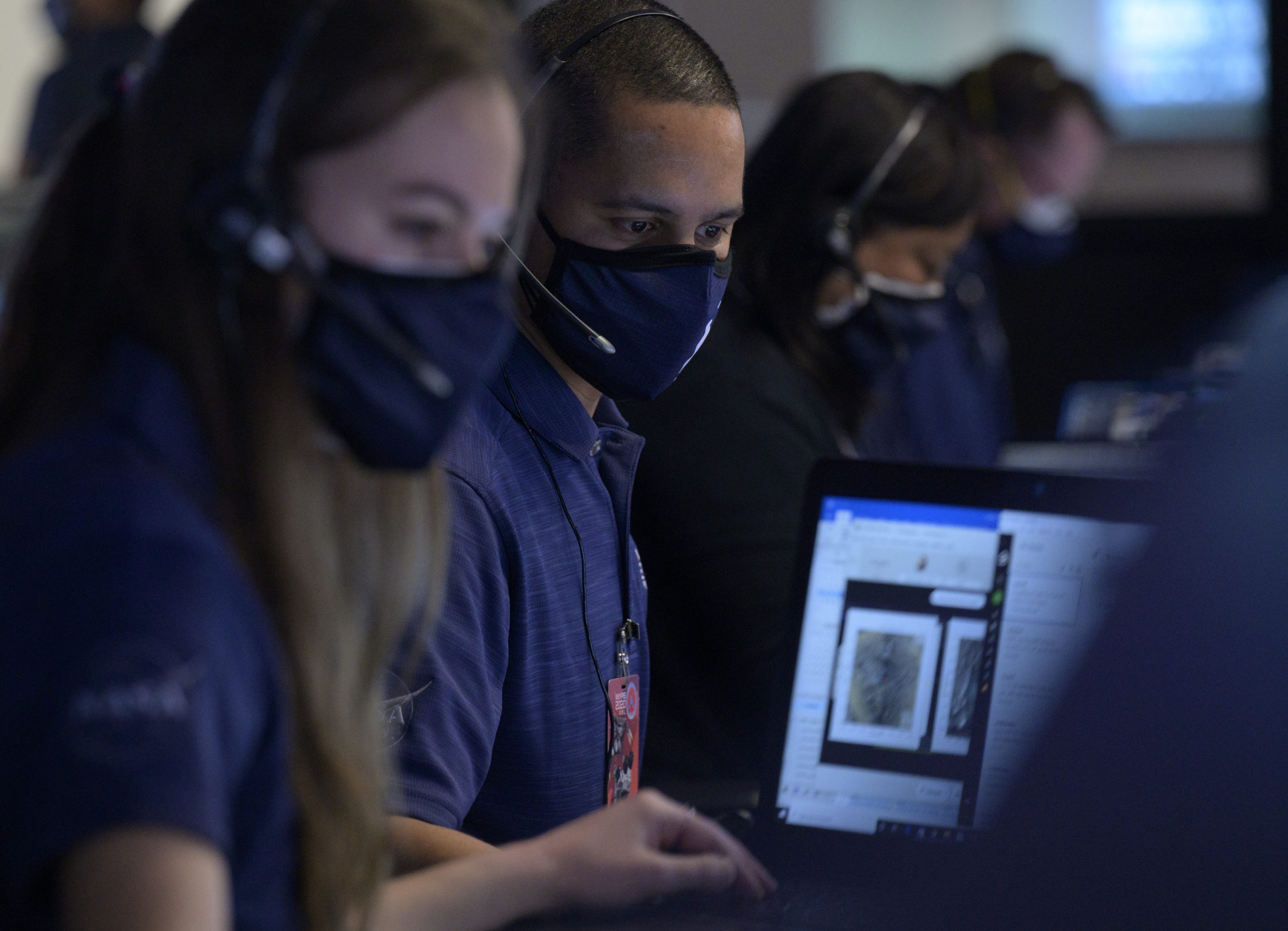 Photo of members of NASA’s Perseverance Mars rover team, a young white woman and a young Black man, study data on monitors in mission control, Thursday, Feb. 18, 2021, at NASA's Jet Propulsion Laboratory in Pasadena, California. 