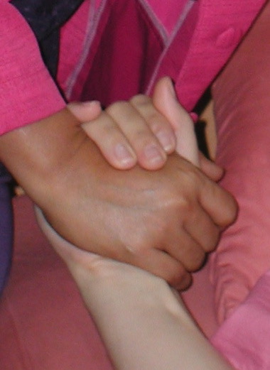 Close up of two hands clasped in support. One hand is dark. The other light.