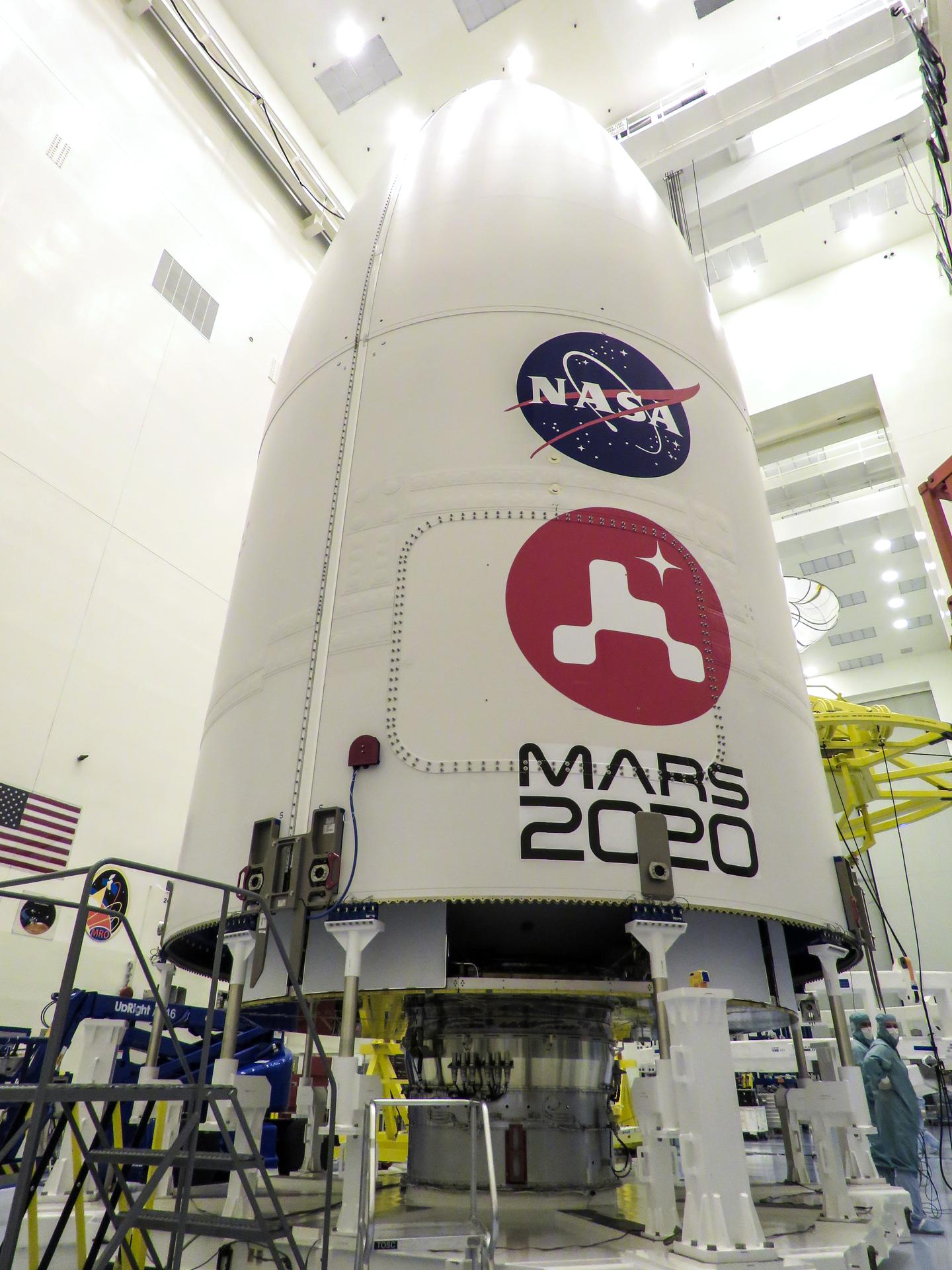 Image of the Mars 2020 logo being installed on the United Launch Alliance Atlas V payload fairing on June 18, 2020 inside the Payload Hazardous Servicing Facility at NASA's Kennedy Space Center. Logo is large red circle with white graphic image of the Perseverance rover and a small, four-pointed star in the upper right quadrant of the circle. Photo Credit: NASA/Christian Mangano
