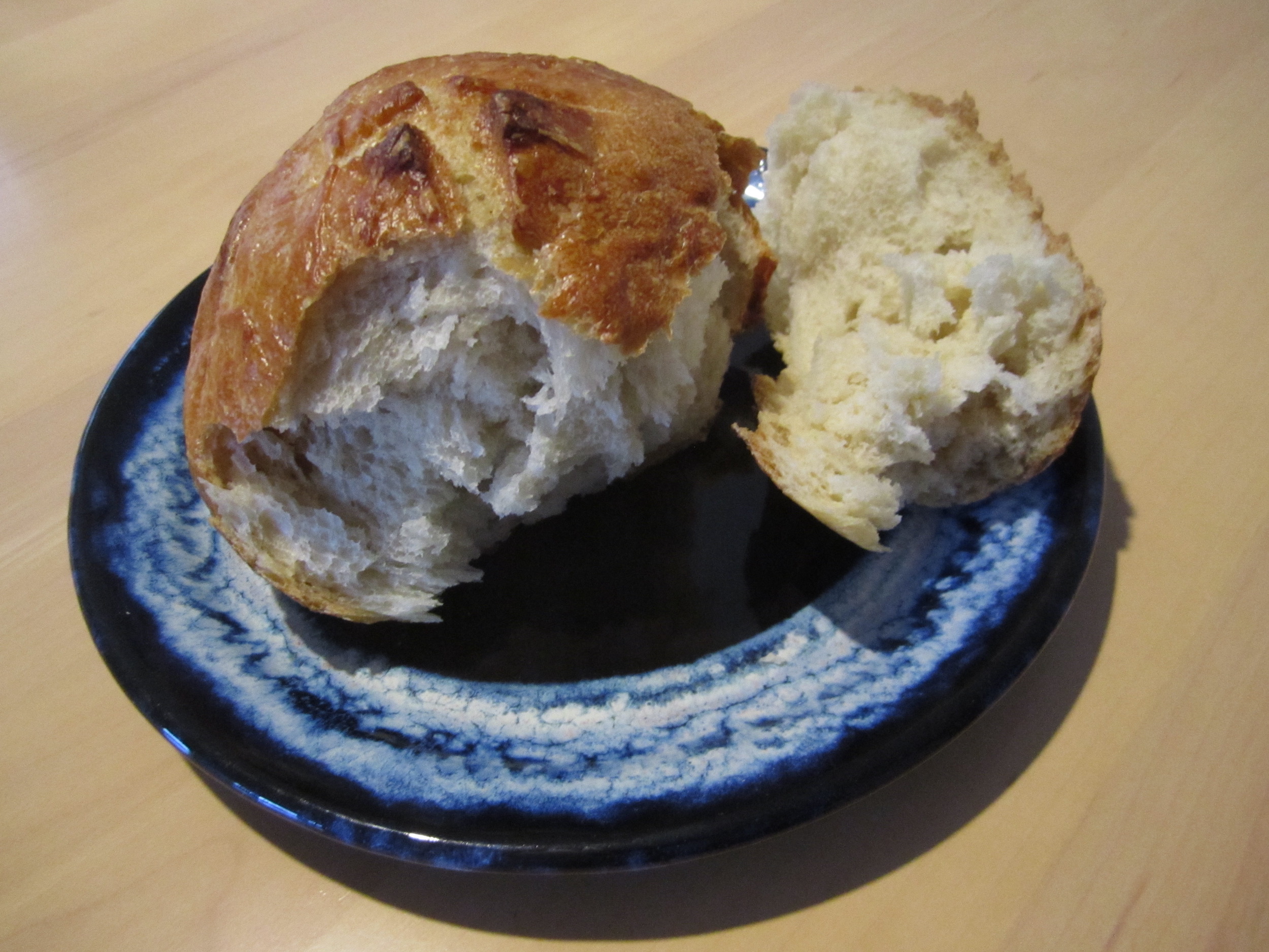 Small, crusty, round roll of white bread, broken, sitting on blue plate