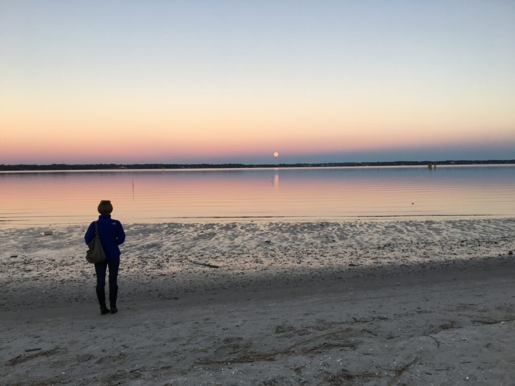 Woman standing on banks of York River looking at the Supermoon on the horizon
